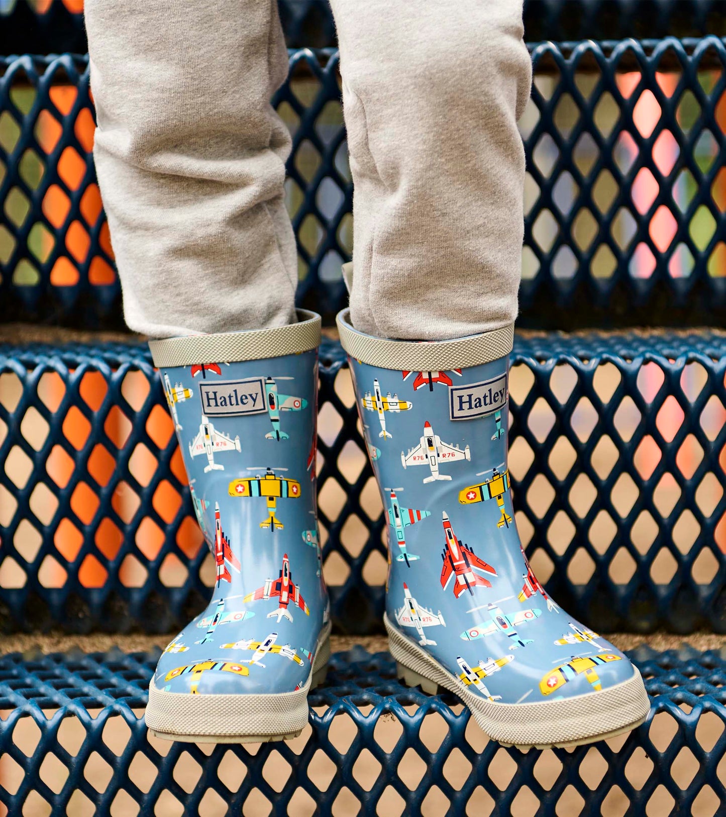 Blue kids rain boots with airplane print and beige soles, shown on a child’s feet from the front
