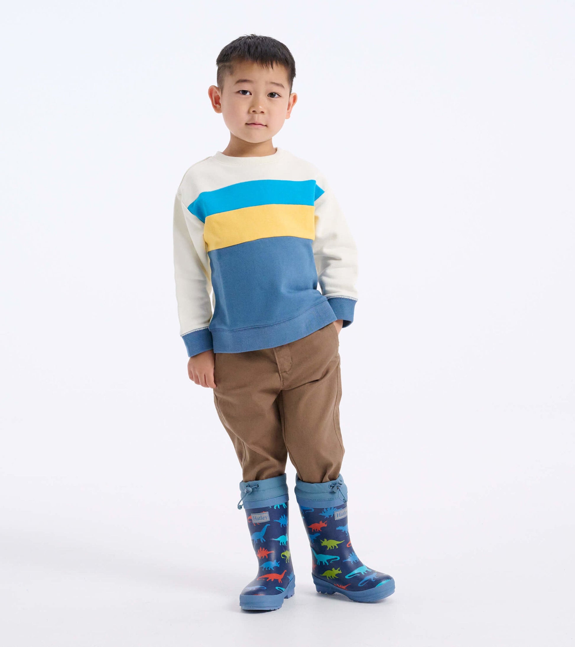 Blue dinosaur-patterned wellies with a Sherpa lining, worn by a child in a colorful sweatshirt and brown pants.