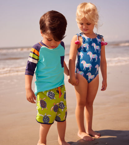 Colorful blue swimsuit with rainbow zebra print and shoulder bows, worn by a girl on the beach.