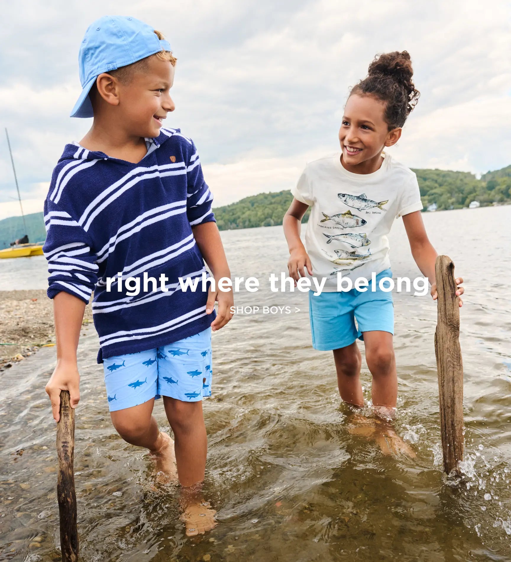 Promotes boys' clothing collection. Showing two children wading in a lake wearing bright summer outfits.