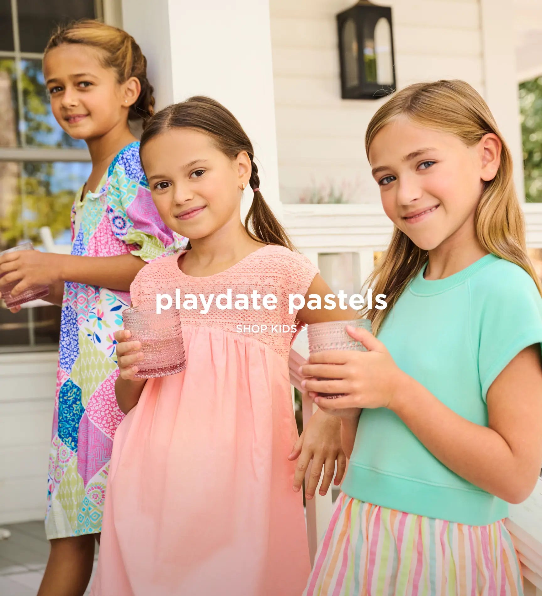 Promotes the kids collection. Showing three girls wearing pastel outfits and holding drinks on a porch.