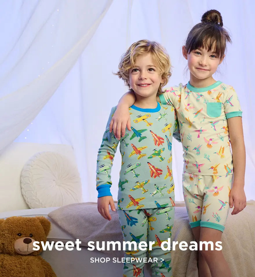 Promotes kids' sleepwear. Showing two children standing in colourful printed pyjamas in a bedroom.
